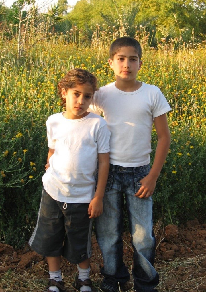 Ziv Hagbi as a child standing with another boy in a sunlit field of wildflowers