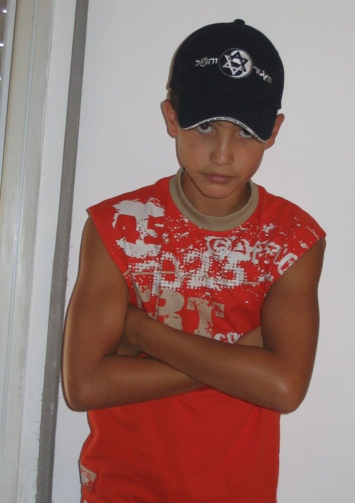 Ziv Hagbi as a boy in a red shirt and baseball cap with a Star of David, arms crossed