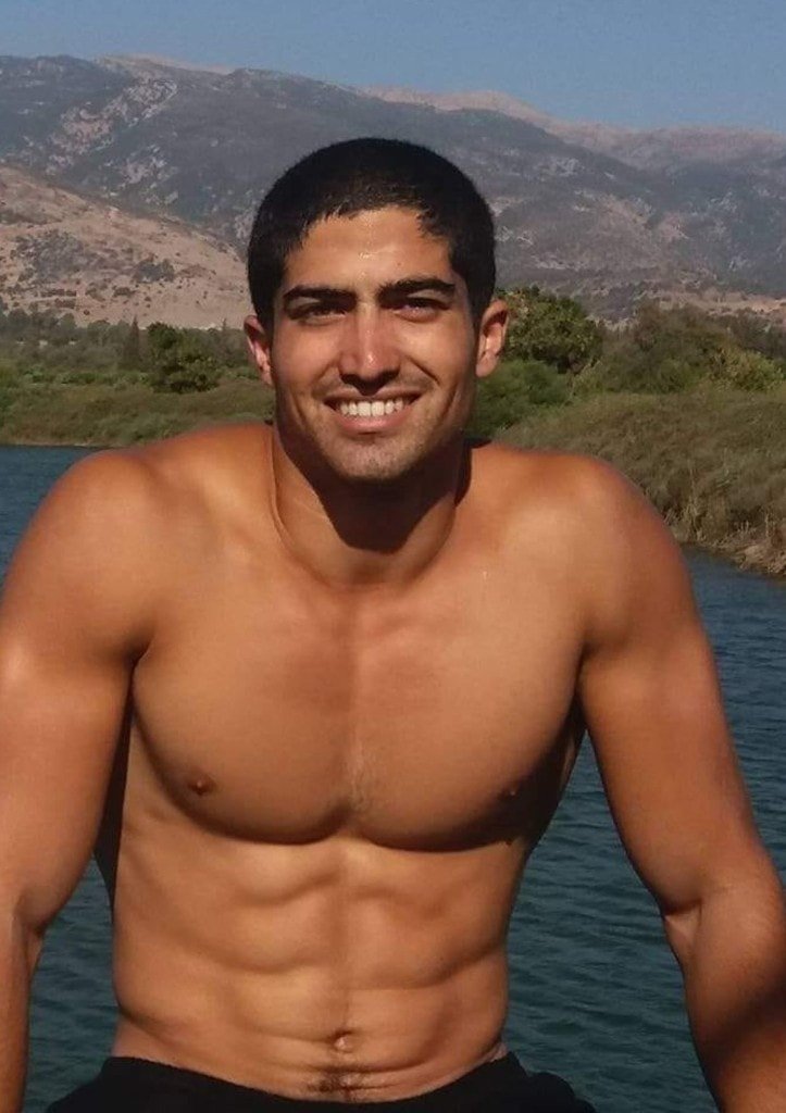 Ziv Hagbi smiling outdoors, shirtless, with mountains and a lake behind him
