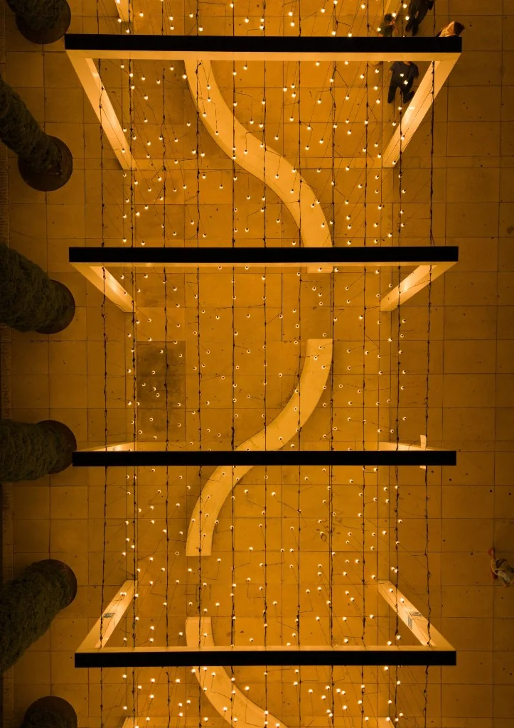 Aerial view of the Light Monument installation with hundreds of warm bulbs hanging above a winding white bench