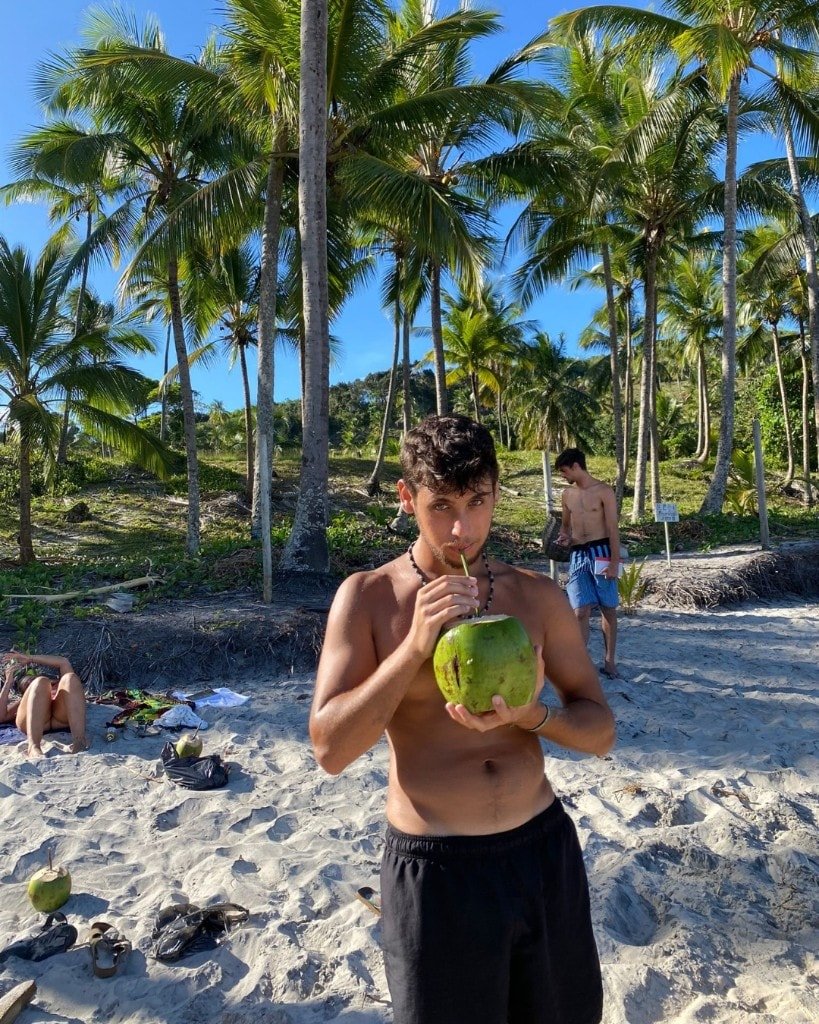 Ron Shemer standing on a beach drinking from a green coconut