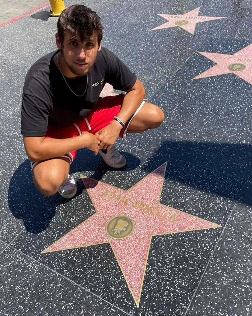 Ron Shemer crouching on a sidewalk beside a Hollywood Walk of Fame star that reads Adam Sandler