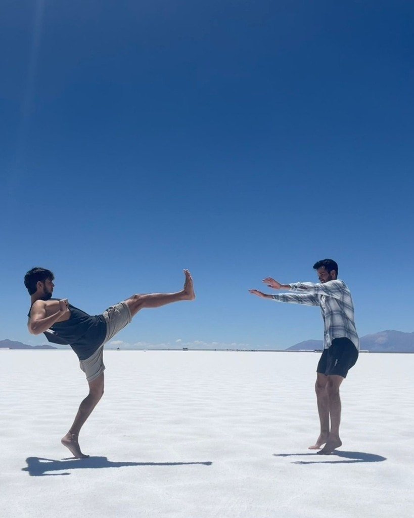 Two young men posing playfully on a white salt flat under a clear blue sky