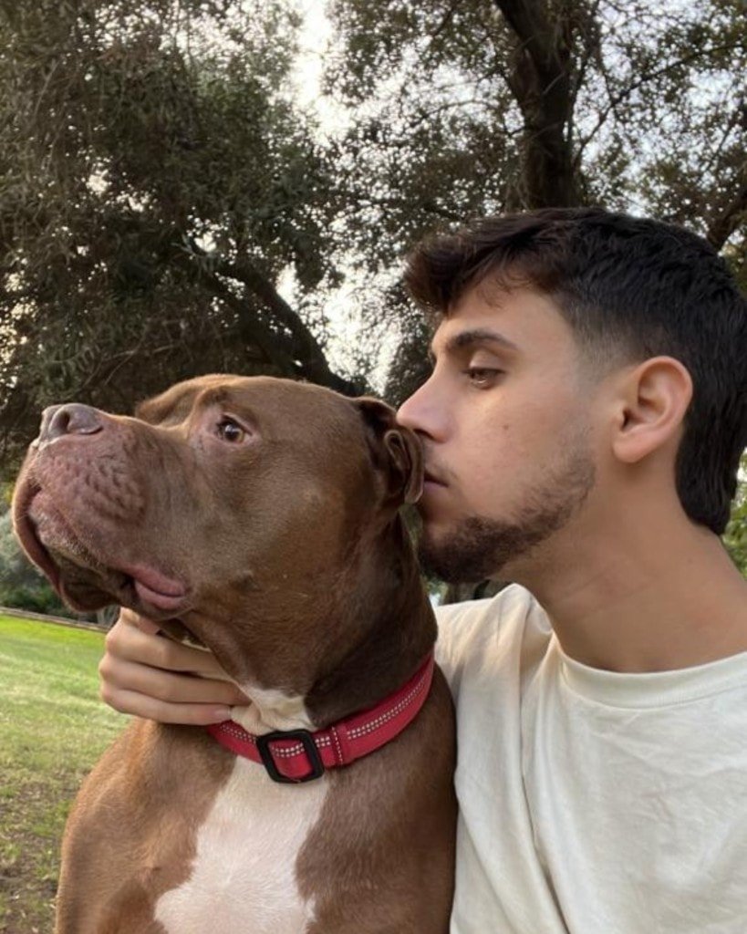 Ron Shemer leaning toward a brown dog with a white chest and a red collar