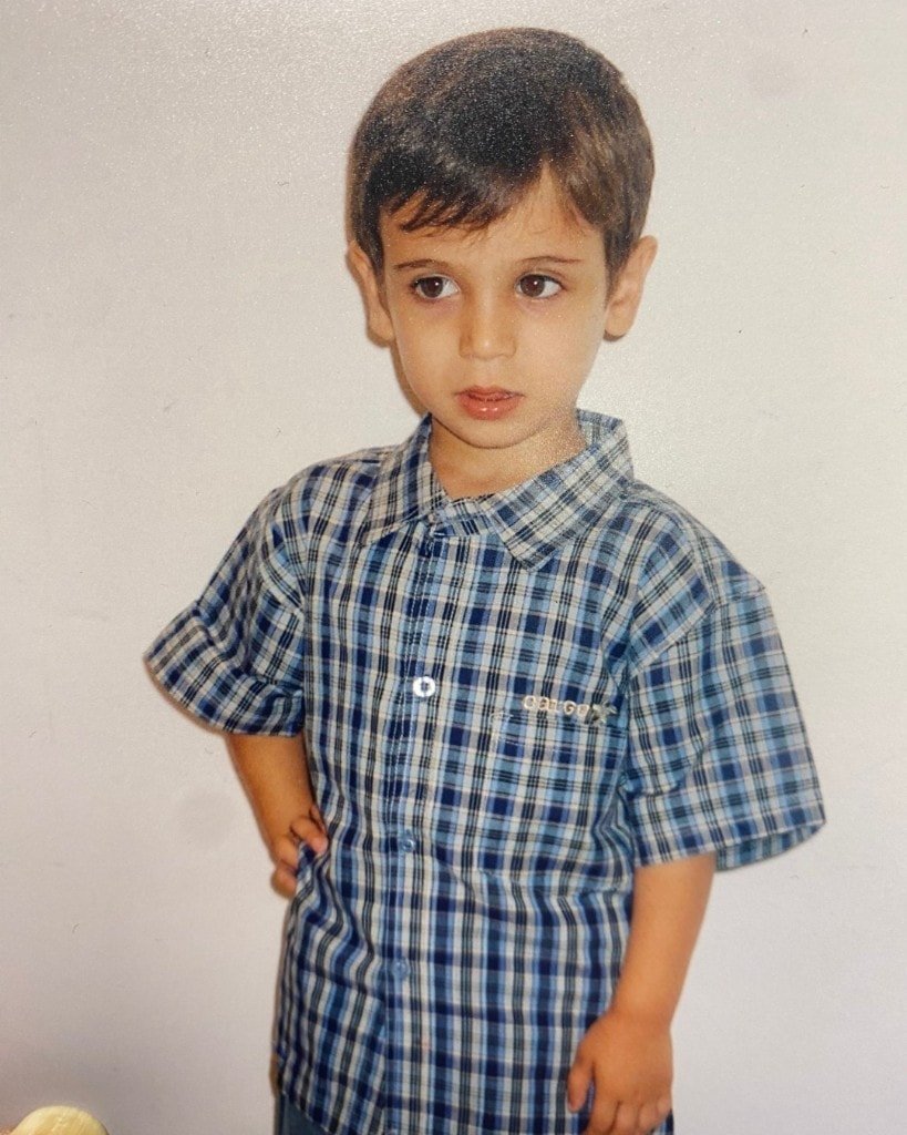 A childhood photograph of Ron Shemer as a young boy in a blue plaid shirt, standing with one hand on his hip