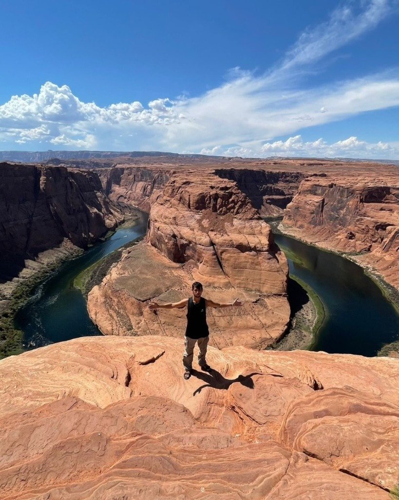 Ron Shemer standing with his arms outstretched overlooking a river bend in a sandstone canyon