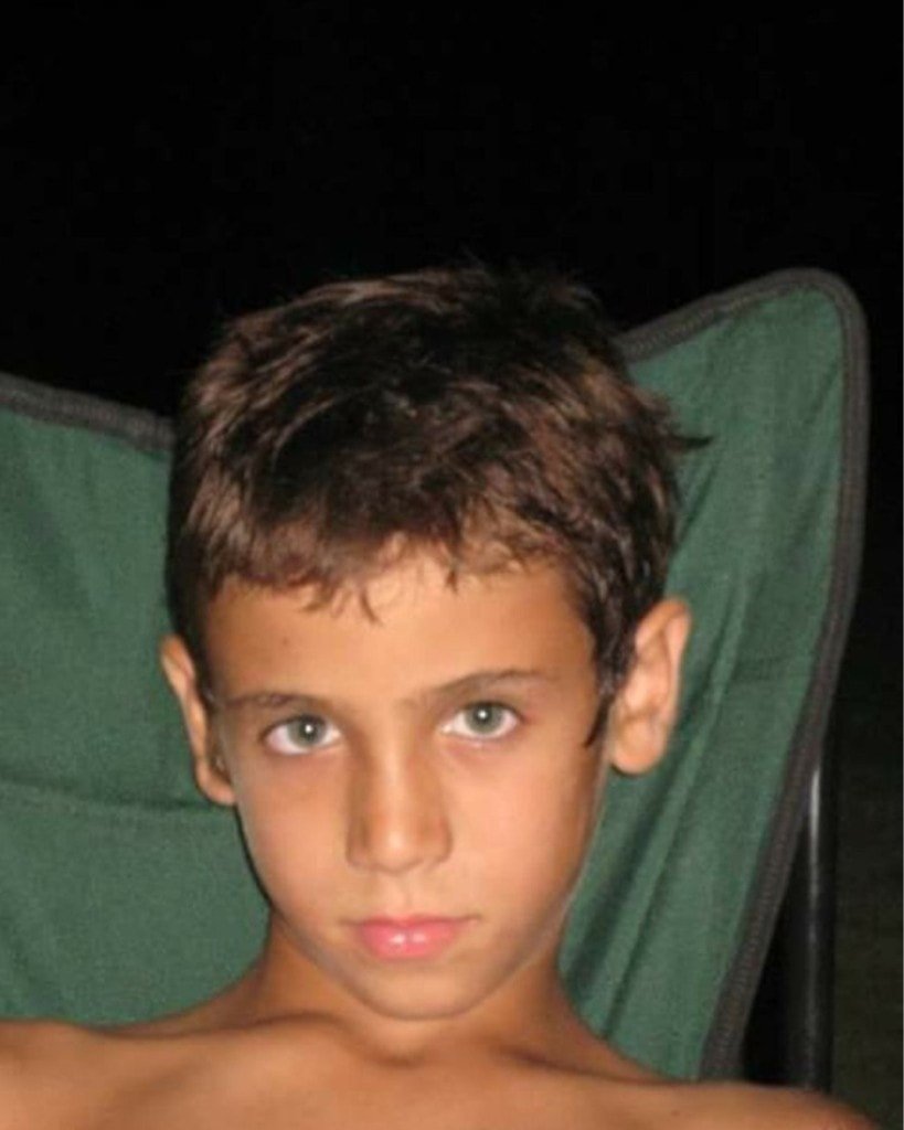 A young boy with short brown hair sitting in a green folding chair